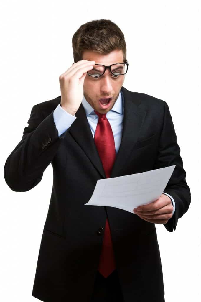 Shocked young business man reads a document he is holding.