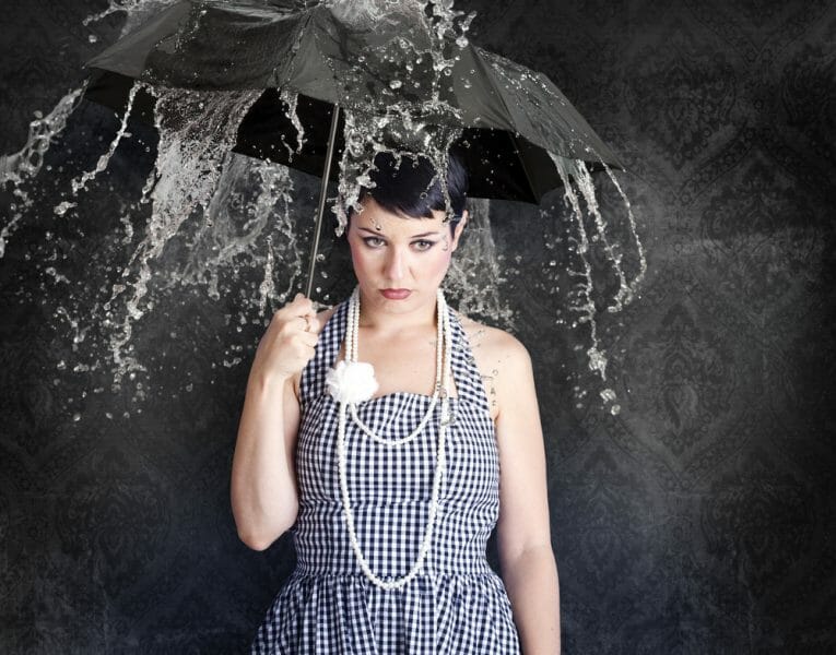 Sad young woman in a dress holding an umbrella over her head as water pours down, didn't have a Plan B if her permanent maintenance didn't come through.
