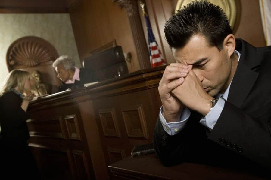 Man in the witness stand holding his head while attorney talks to judge on the bench