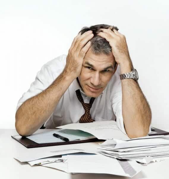 Harried man with a pile of bills and paperwork in front of him, holding his head.