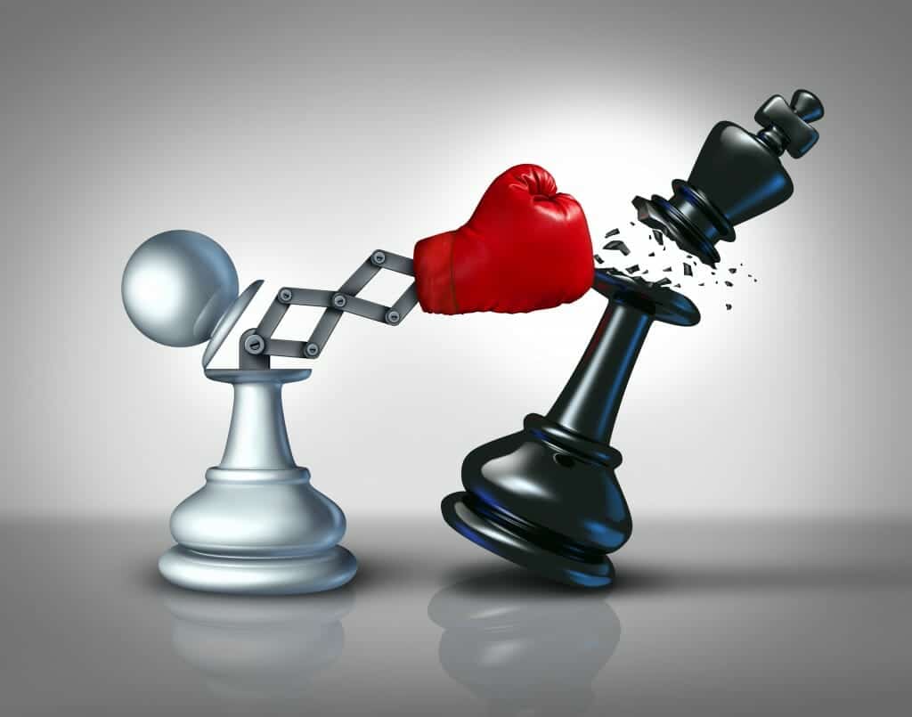 Boxing glove shooting out of white pawn chess piece knocking the head off a black King chess piece.