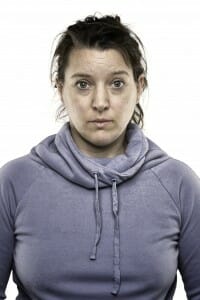 Woman with dirty hair and no makeup wearing a hoodie.