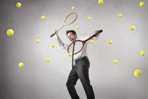 Man holding tennis rackets in each hand wildly batting multiple tennis balls coming at him. Divorce stress