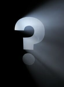 Question Mark cut in black cardboard with a light shining through it.