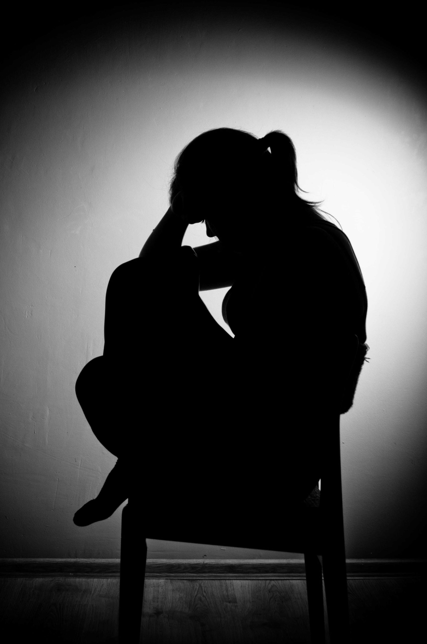 Silhouette of a depressed young woman holding her head.
