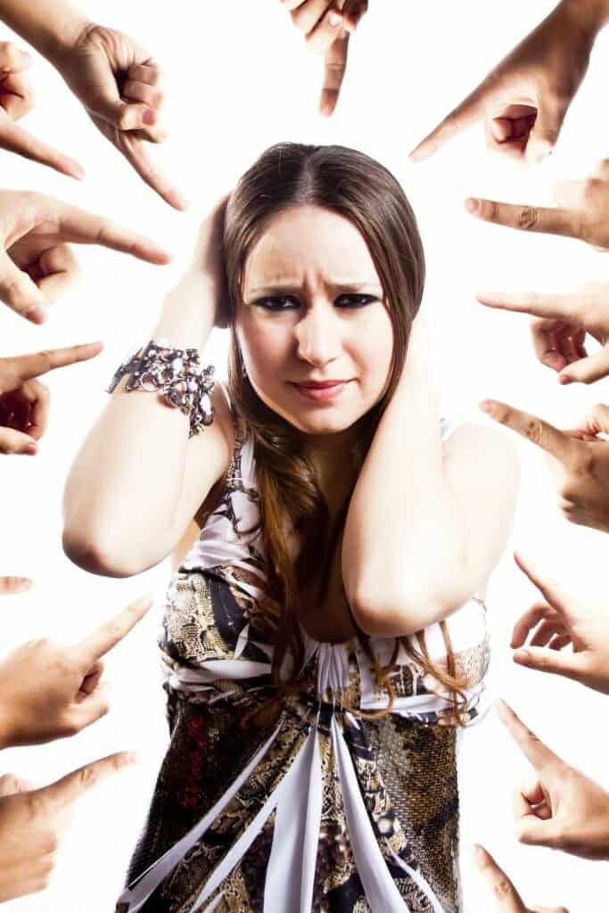 Confused woman holding her head with many fingers pointing at her.
