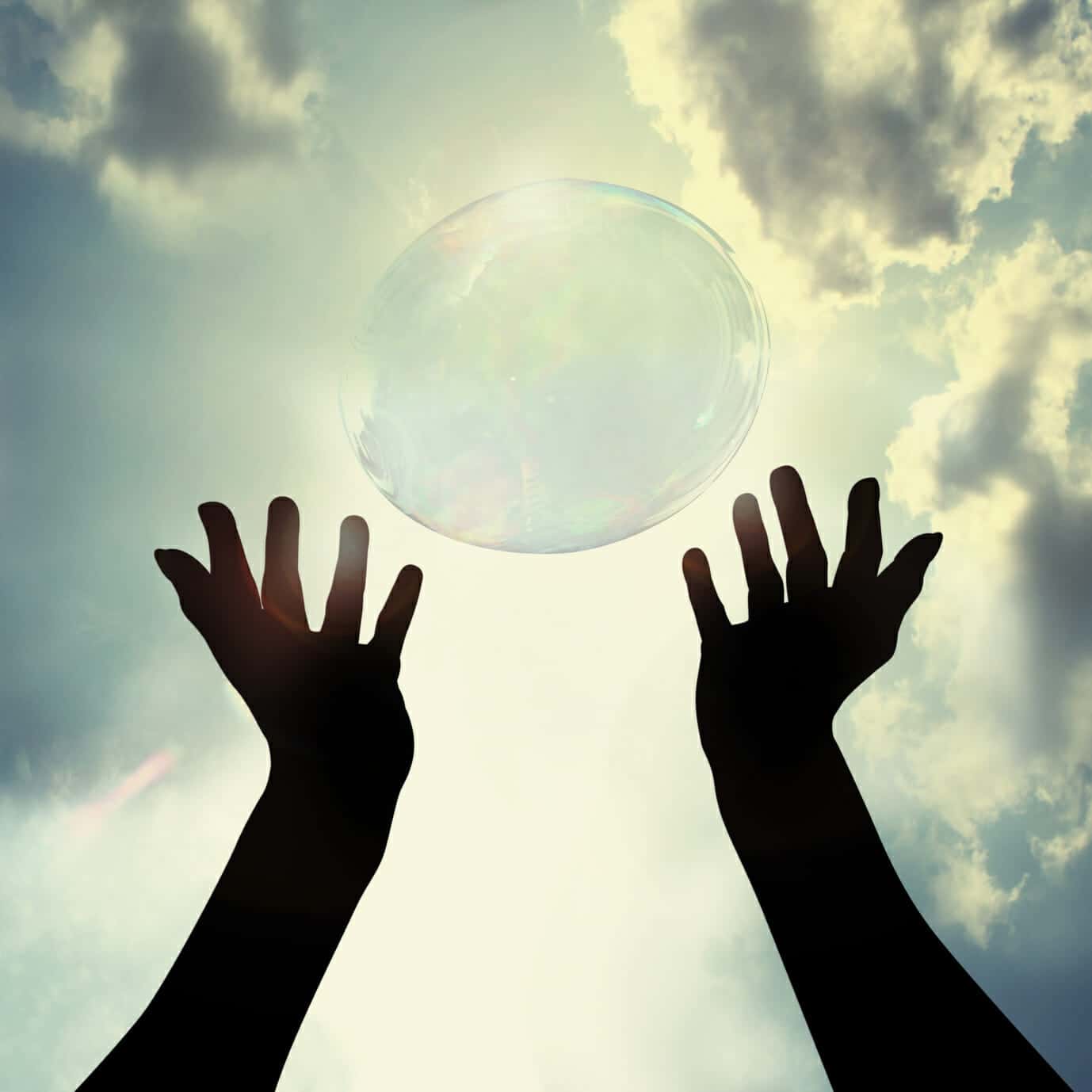 Hands reaching up to a blue sky, releasing a bubble. Sun is shining.