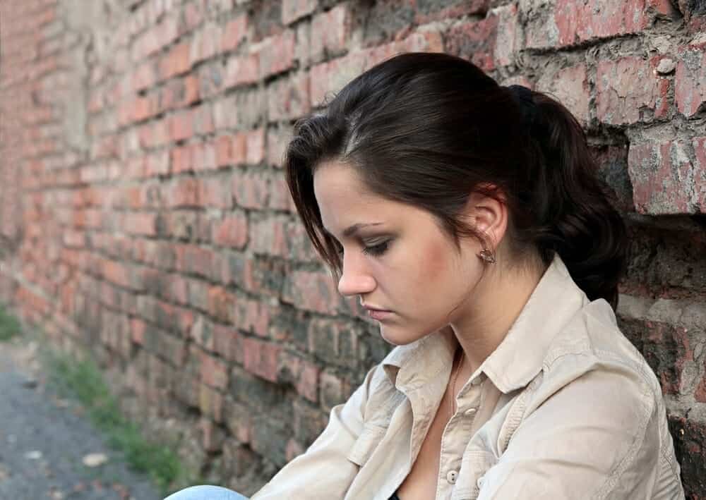Sad woman on a divorce guilt trip sitting against a brick wall.