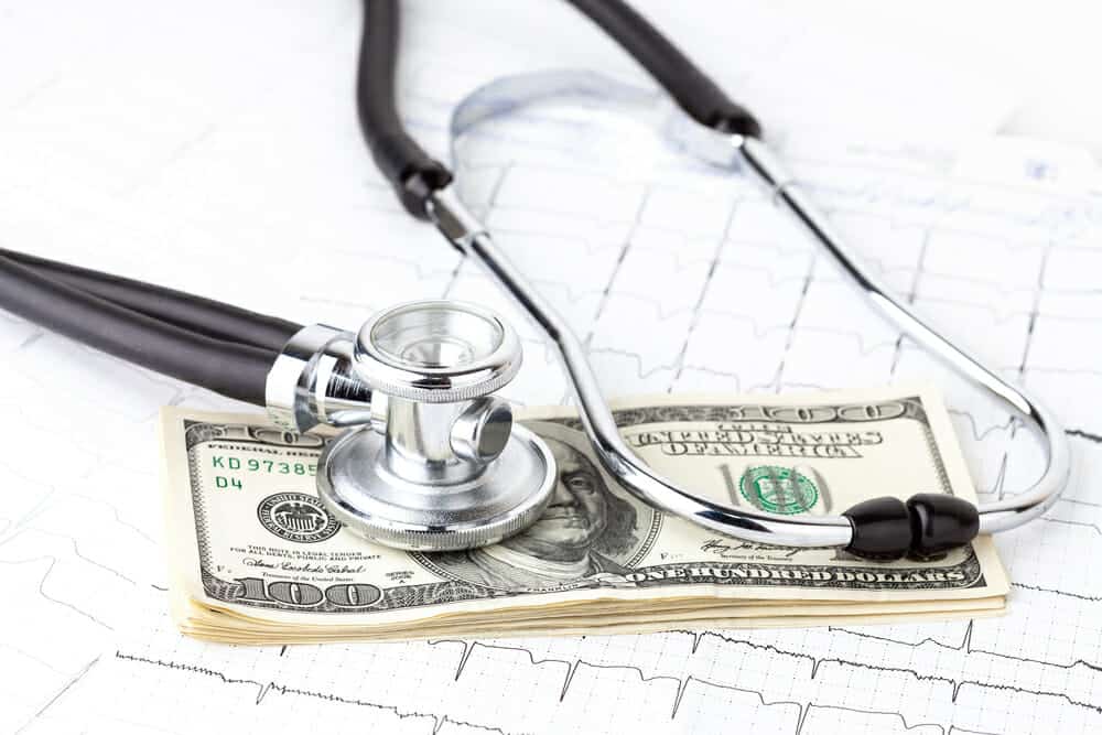 Stack of $100 bills on EKG graph with a stethoscope on top.