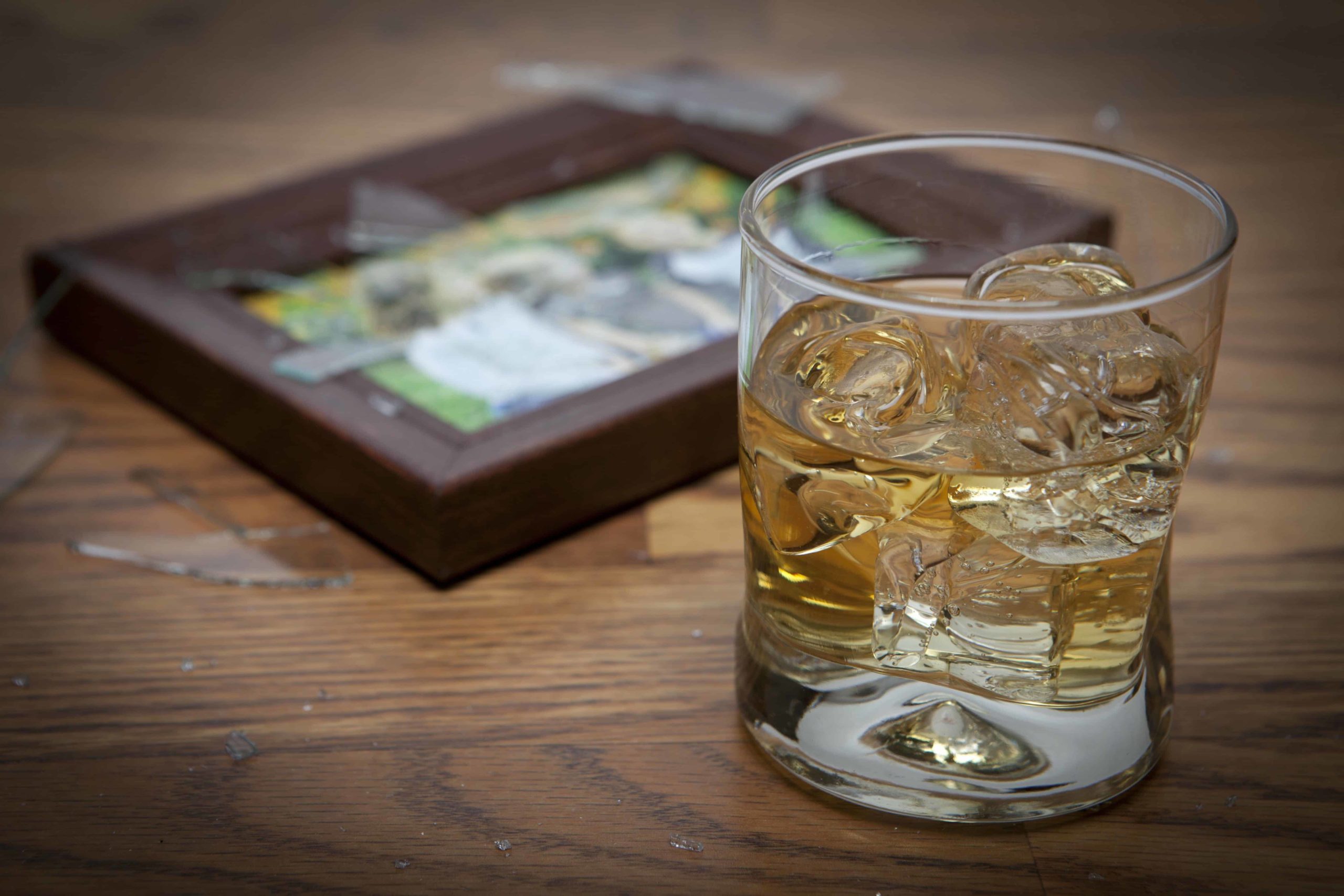 Glass of liquor on the rocks in front of a picture of a family with shattered glass