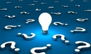 Illuminated light bulb on a blue background full of question marks