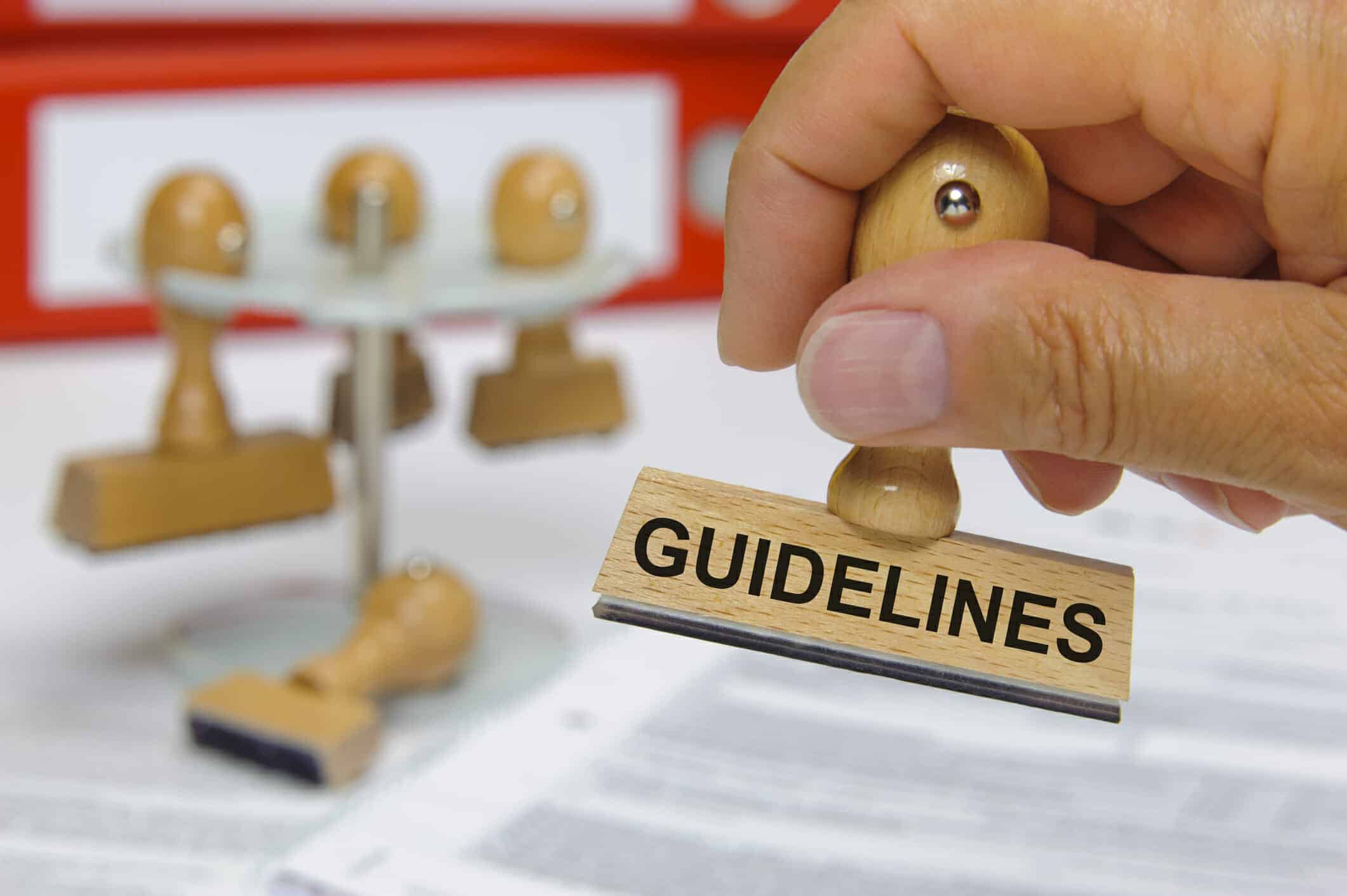 Hand holding rubber stamp with the word "guidelines" on it
