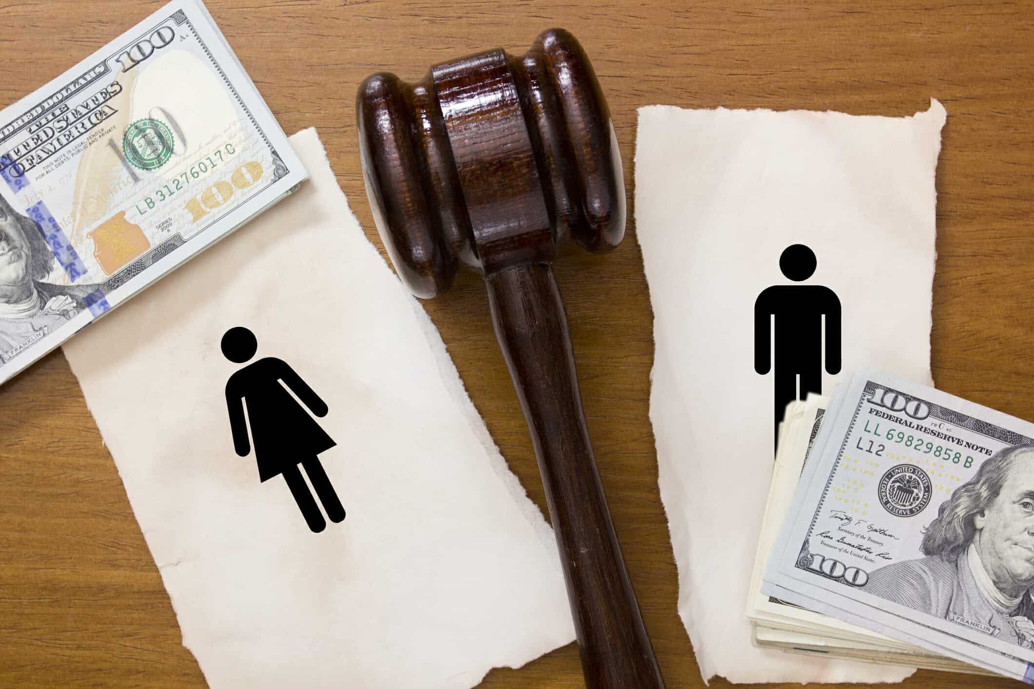 Paper with figures of a man and a woman on it, torn in half with a gavel dividing the sides and stacks of $100 bills next to it.