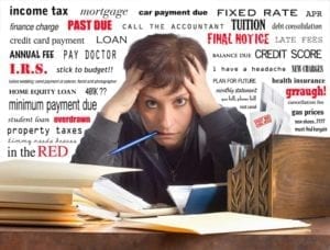 Harried woman surrounded by paperwork with words IRS, Past Due, Overdrawn, Credit Score etc in the background.