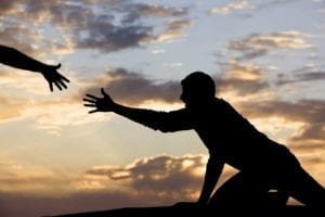 Silhouette of a man reaching out in the sunset. Another hand reaches for him.