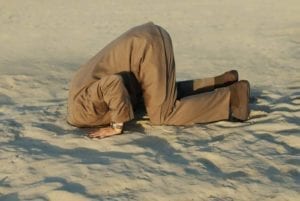 Business man kneeling down in the desert. Burying your head in the sand is not a good strategy.