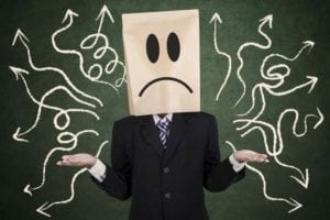Person with bag over head and a confused face standing in front of a chalkboard with arrows on it pointing every which way.