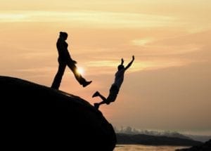 Silhouette of woman kicking man off a boulder into a river at sunset.