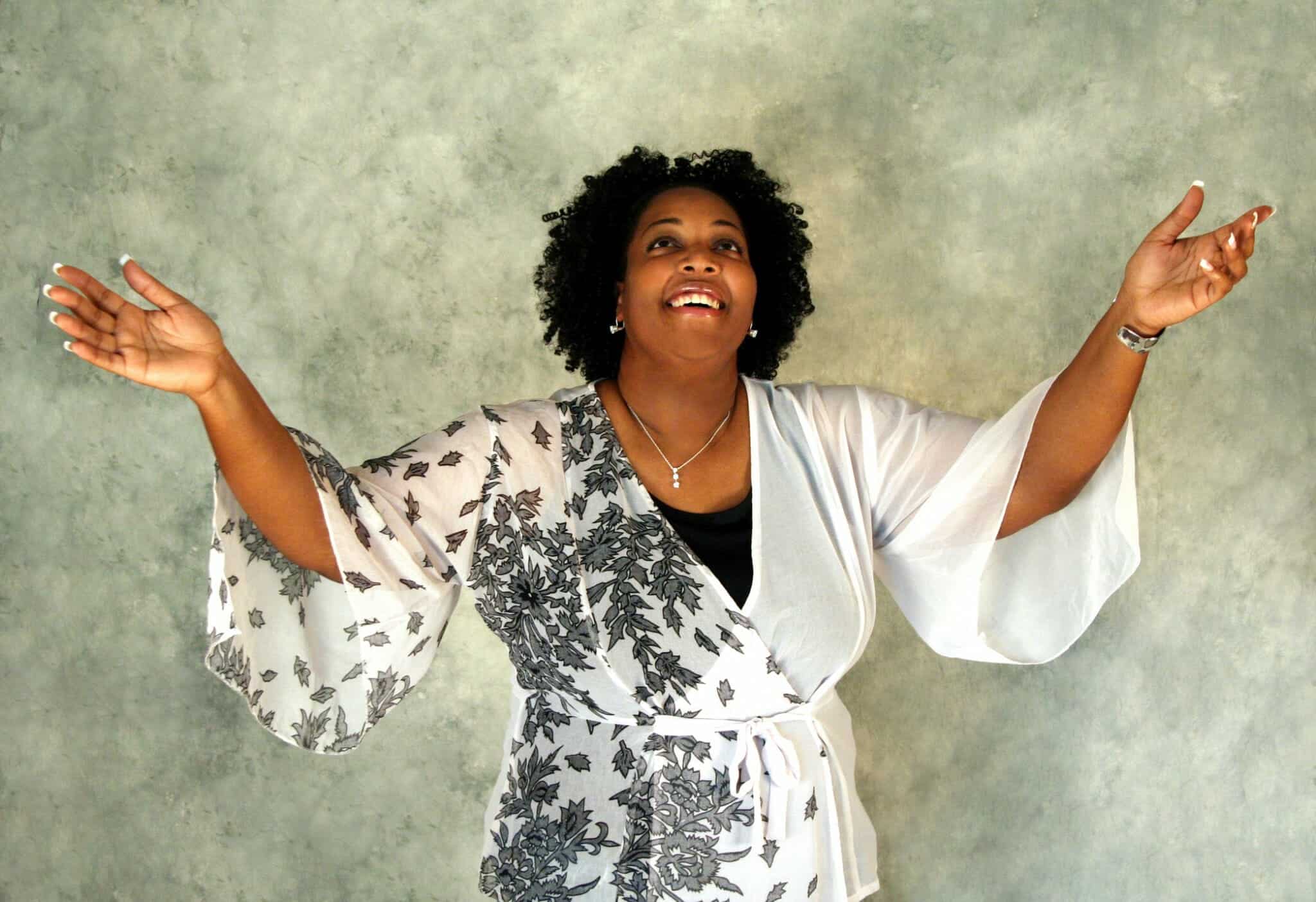 Grateful, smiling African American woman reaching her hands to the sky