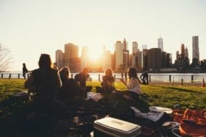 Girl friends having a picnic in a small park next to a river in front of a city