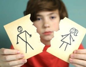 Sad boy whose parents are fighting over equal parenting time holding up torn stick figure picture of parents