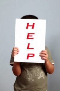 Sad boy with divorced parents holding a help sign in front of his face.