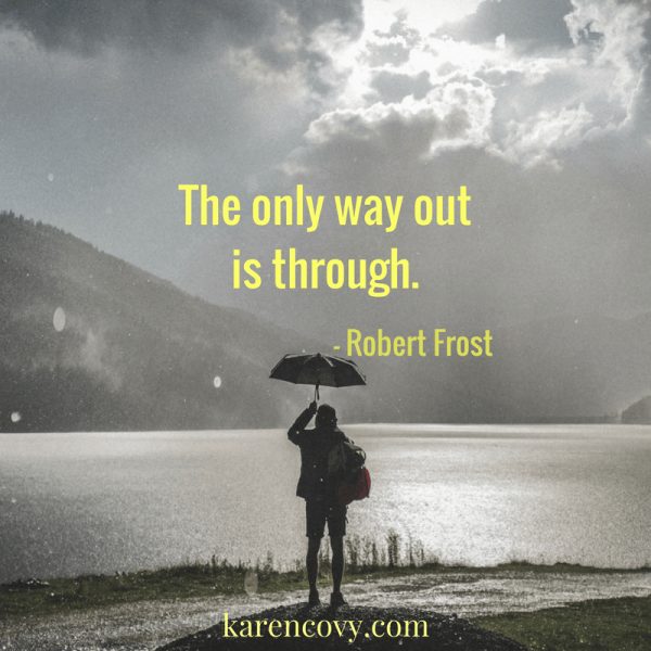 Woman standing on a river bank in the rain with the saying: "The only way out is through."