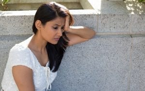 Upset sad young woman in white dress sitting on bench isolated gray background. Negative emotion facial expression feeling body language