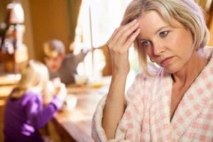 Harried mother holding her head with kids in the background. Parenting after divorce is hard!