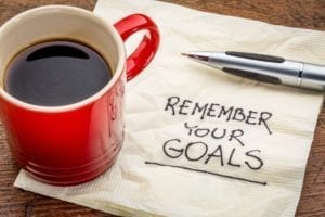 How to Set Goals and Use Them: Red coffee mug sitting on a napkin with the words "Remember Your Goals" written on it.
