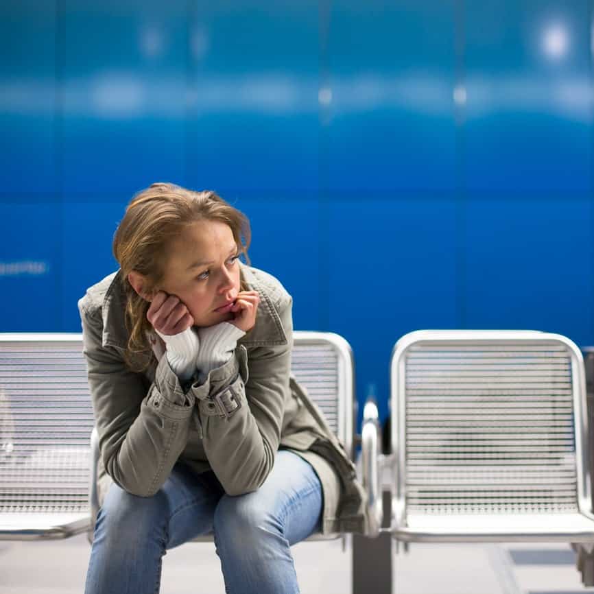 Lonely woman facing divorce sitting on aluminum bench outside against a blue background.