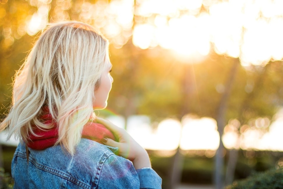 Confident blonde woman in blue jean jacket looking toward the sun.