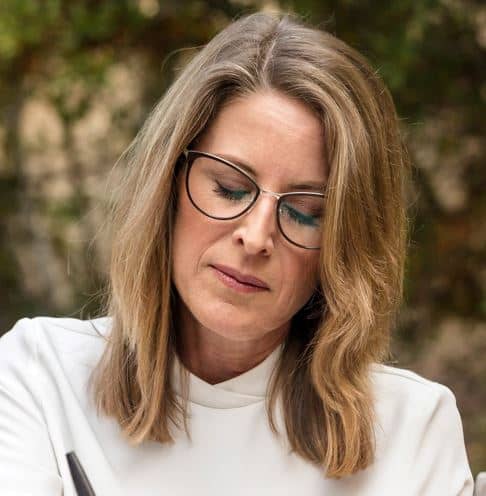 Middle aged woman with glasses looking down and writing.