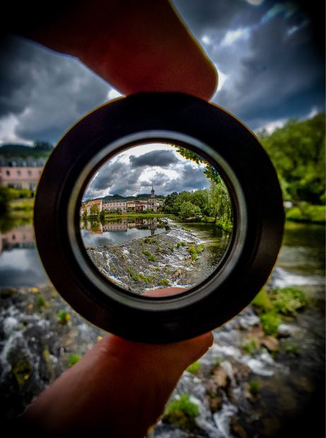 Fingers holding up a camera lense that changes what you see. The power of focus.