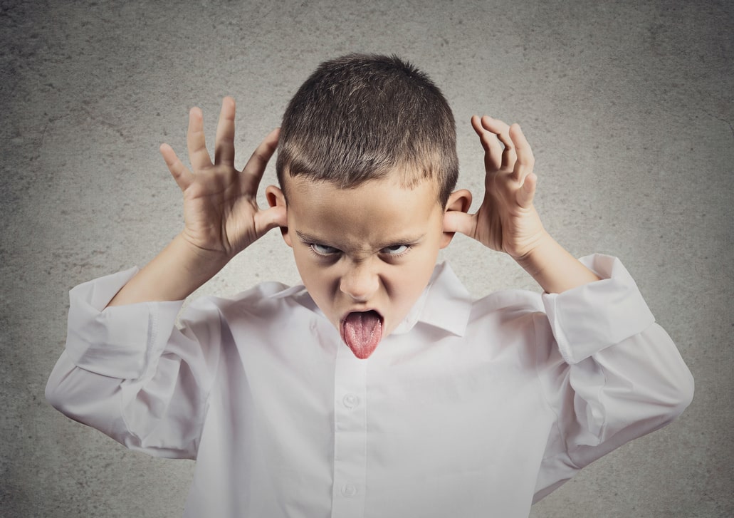 Young boy with his thumbs in his ears making a face and sticking out his tongue. Take control of your kids.