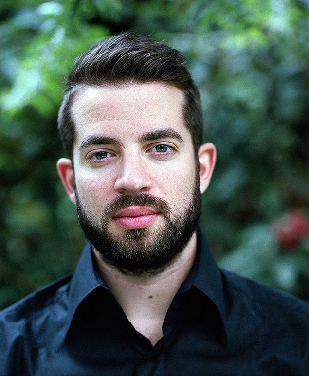 Young white man with dark hair and a beard looking at the camera