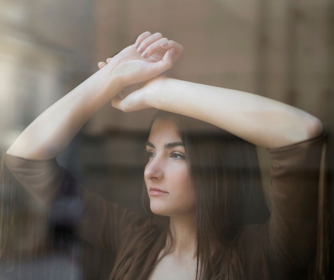 Pretty but [ensive woman who is afraid to divorce looking out from behind glass window.