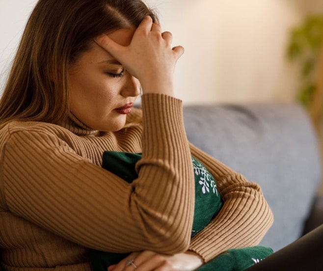 Pretty Hispanic woman in a brown turtleneck looking down with her hand on her forehead while deciding to divorce.