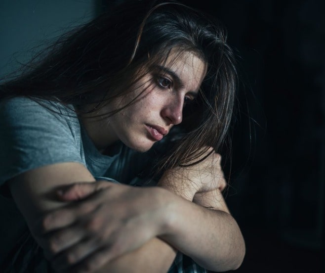 Beautiful upset woman who has a fear of divorce curled up in a dark corner trying to decide what to do.